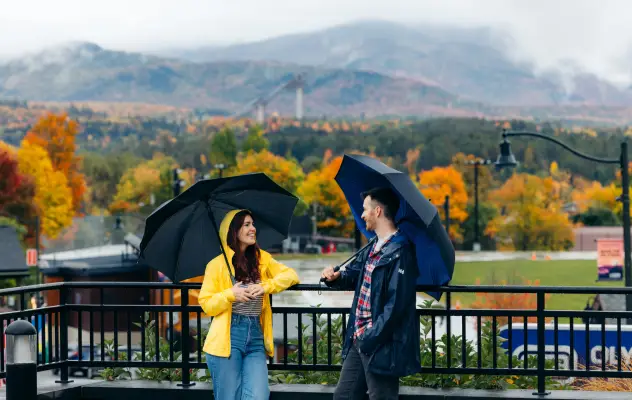 A man and woman stand on a balcony overlooking mountains covered in foliage.