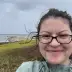 A woman with windblown hair smiles in front of a grey coastline.