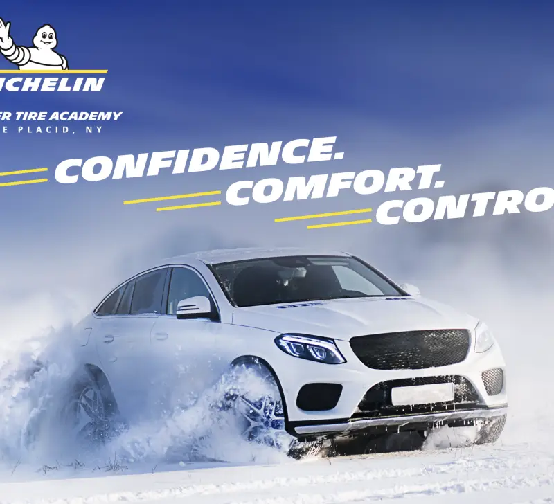 White sedan drives in snow with Michelin logo and the words Confidence, comfort, and control above it against blue sky