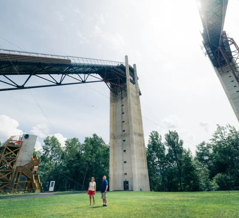 Senior couple stands on grass at the base between two towering ski jumps