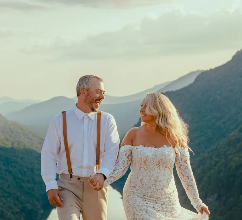 Smiling bride and groom with the valley and mountains surrounding them in the background