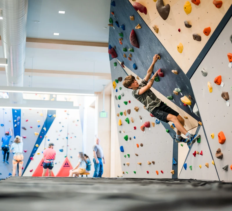 A teenage boy climbs a cantilvered indoor rock climbing wall.