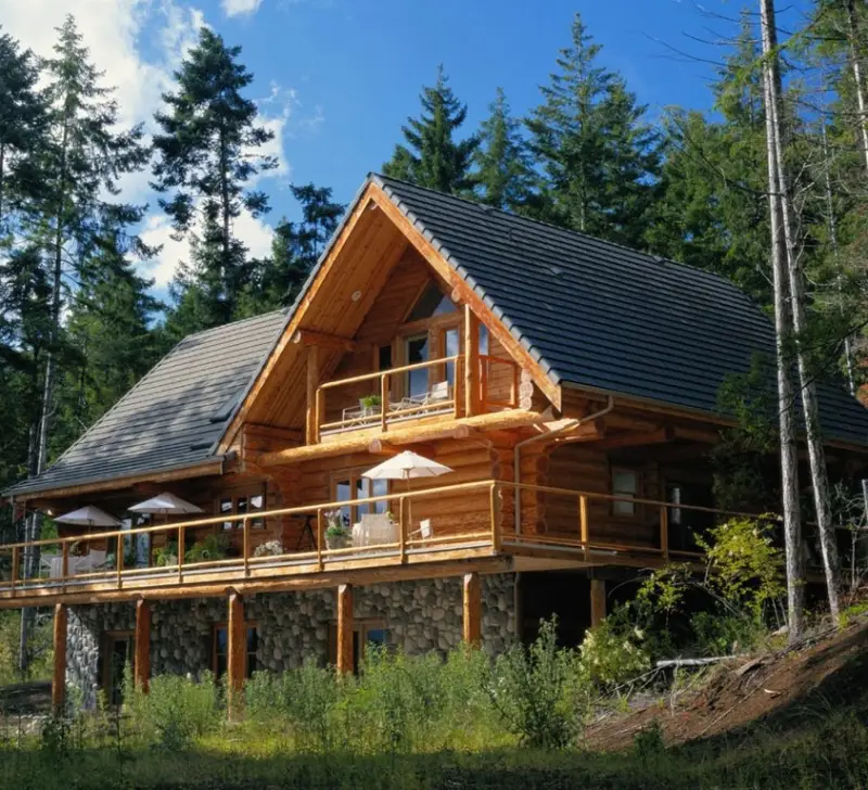 The exterior of a three story log cabin with wrap around deck and balcony above
