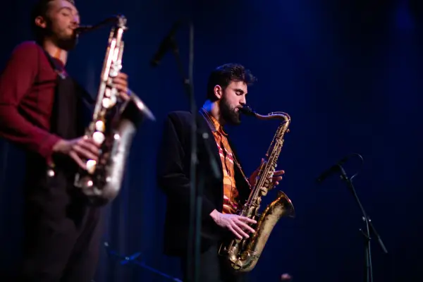 Two people playing the saxophone on a stage. 
