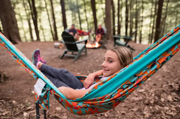 A girl sits in a hammock at a campsite. 