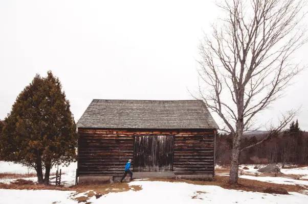 a person walks past a historical barn in the snow. 