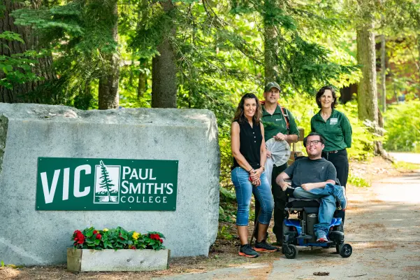 A tour group poses with the welcome sign for Paul Smith's College. 
