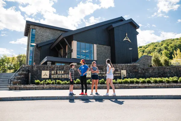 A family stands in front of a modern Olympic lodge in summer.