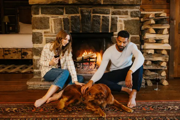 A couple sitting in front of a fireplace with their dog.