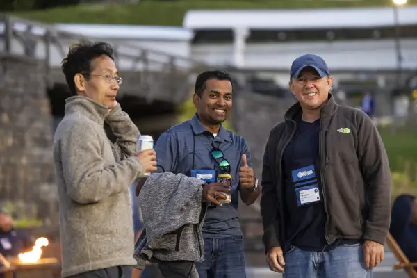 Three men smile at an outdoor IT conference. 