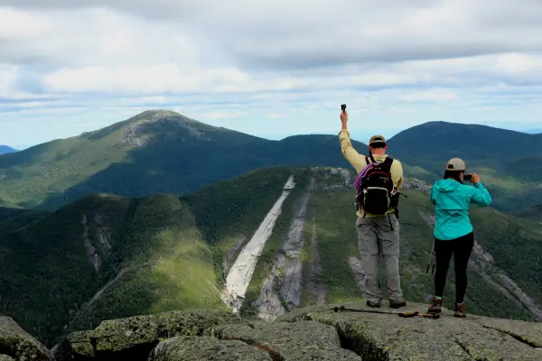 Two people on an open, rocky summit with views of big mountains