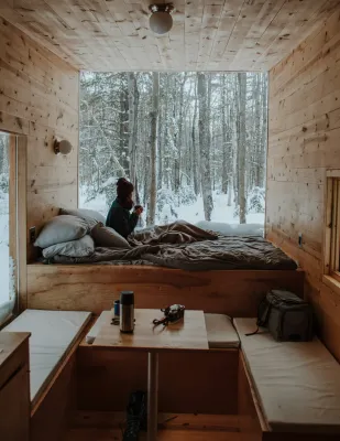 A woman cozies up in a rustic cabin looking out to a winter scene.