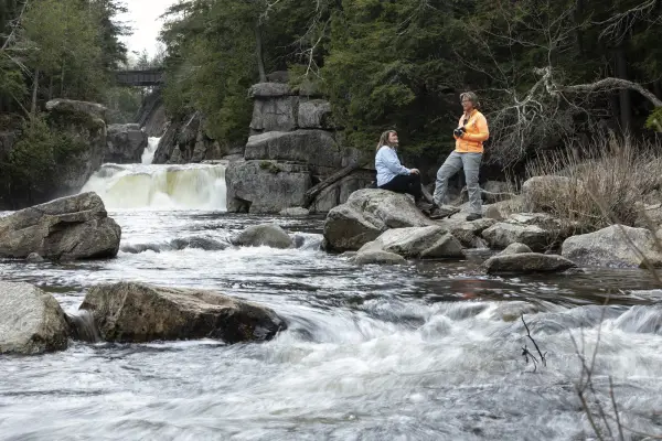 Two women in front of a narrow waterfall.