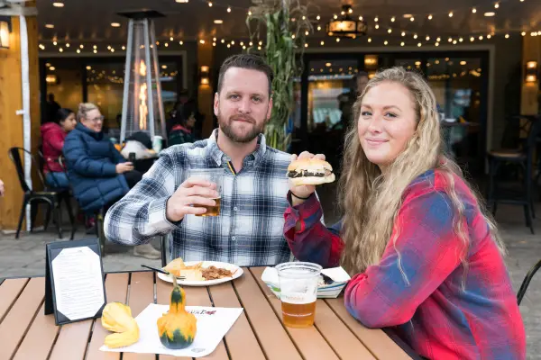 A man and woman share food and drinks at a fall festival. 