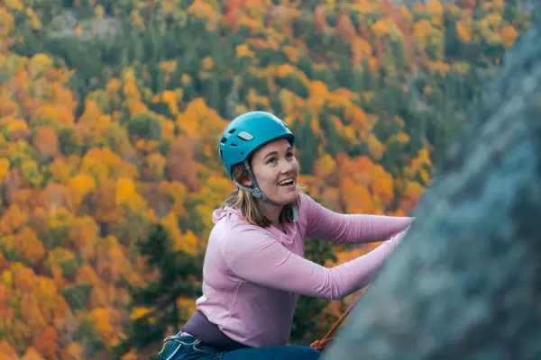 A rock climber with the backdrop of fall foliage behind her,