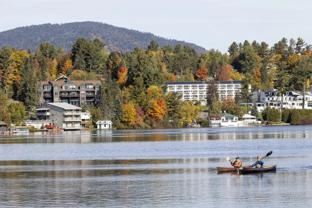 A couple paddles in kayaks on a lake surrounded by resorts.
