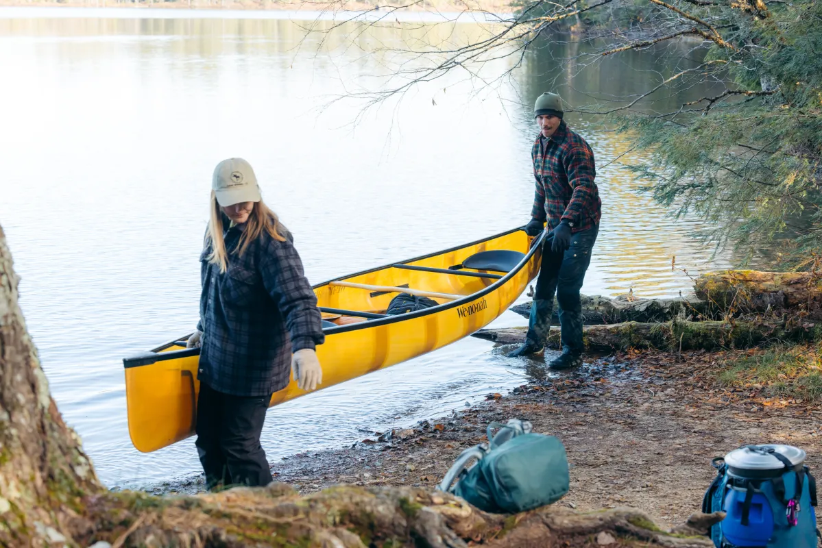 Two people carrying a canoe to a campsite