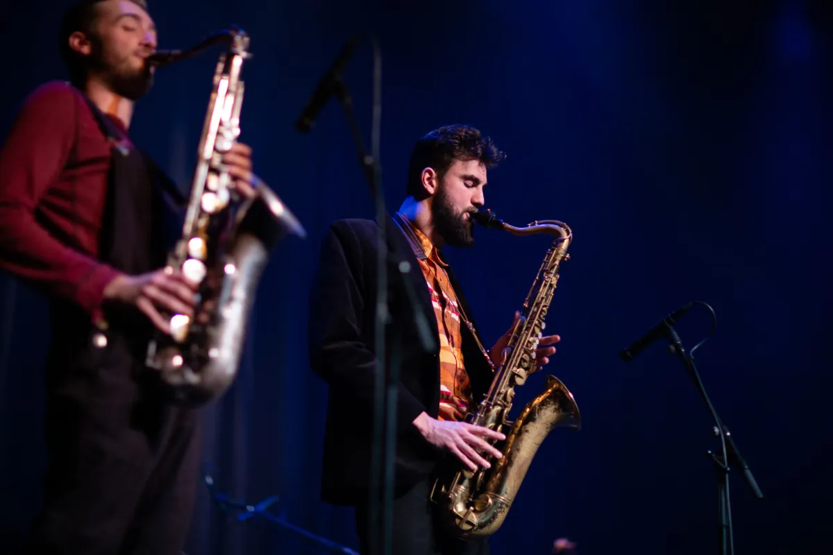 Two people playing the saxophone on a stage. 