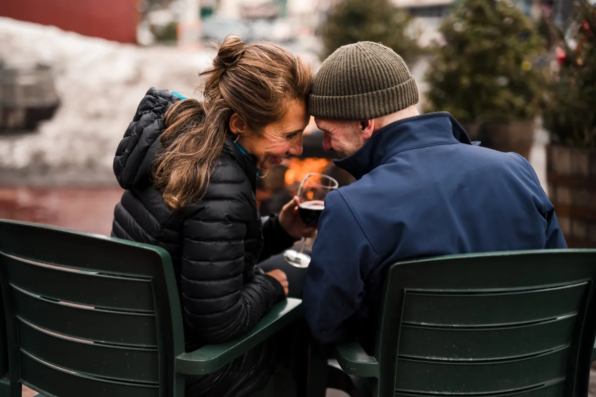 A couple sitting on a patio in the winter in front a fire.