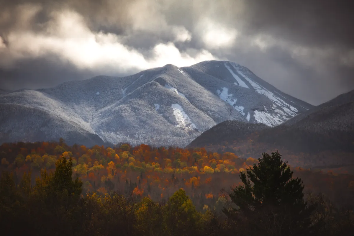 A mountain covered in snow towers over fall foliage.