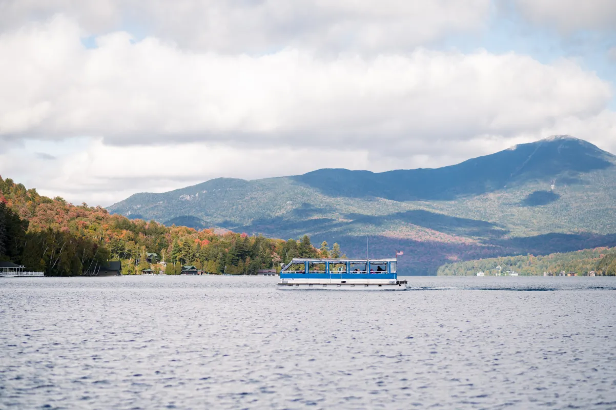A pontoon boat passes in front of mountains covered in fall foliage.