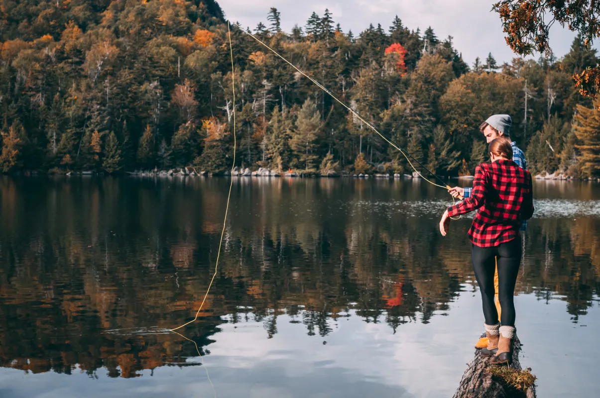 A couple fishes on a lakeside in fall.
