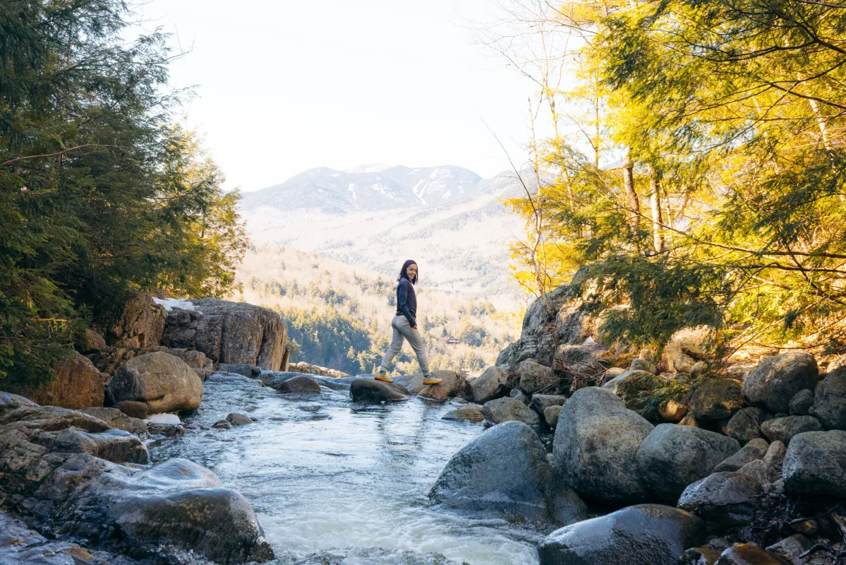 A woman hiking across a spring stream.