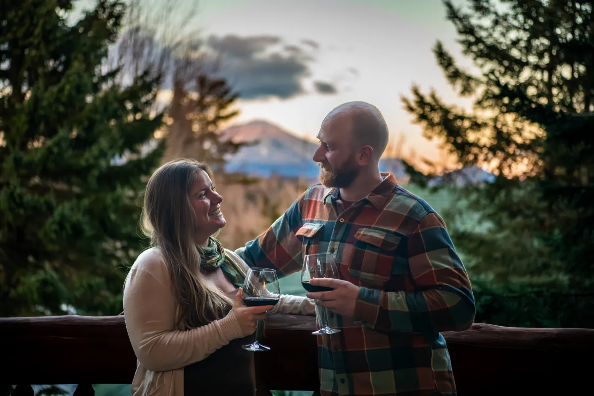 A man and woman cheers wine together on the patio of a lodge. 