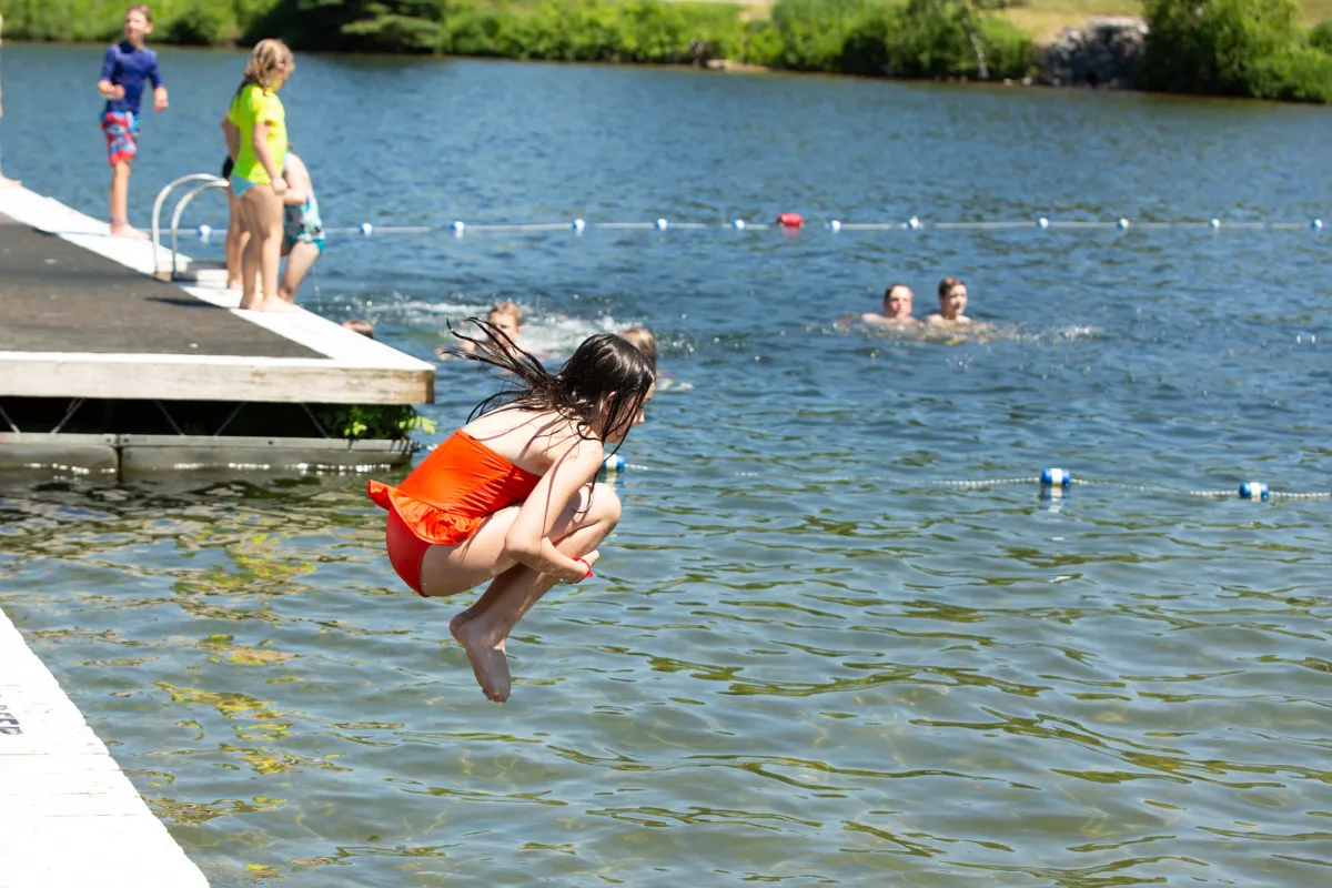 A young girl jumps into a lake in an orange bathing suit. 