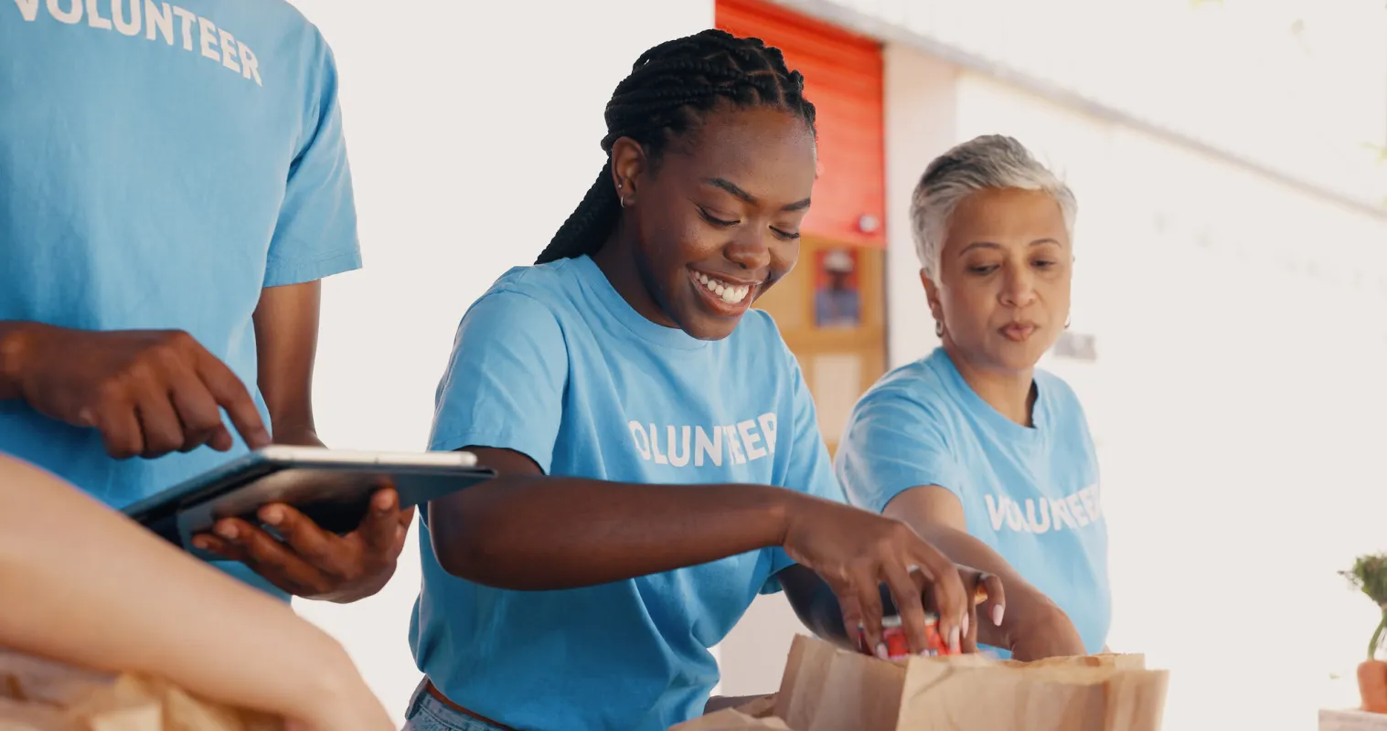 A black woman puts cans in a paper bag for charity. 