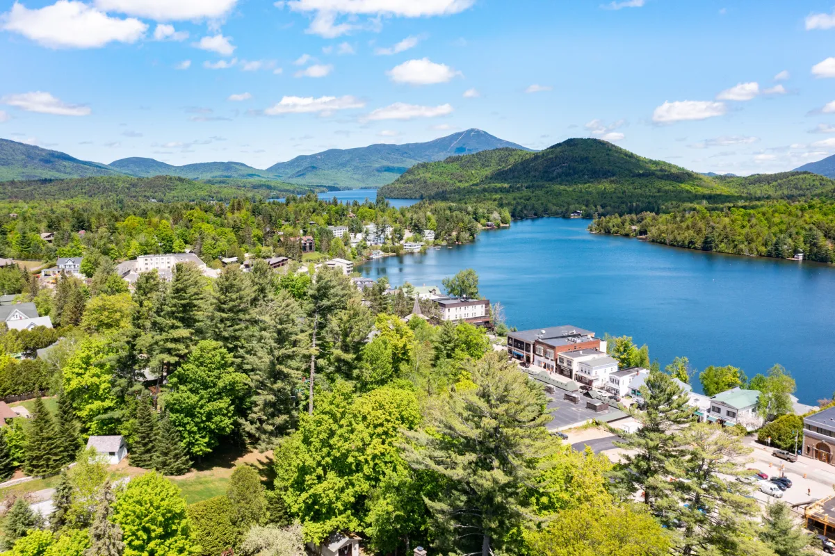 An aerial view of a lakeside town with mountains in the distance on a sunny summer day.