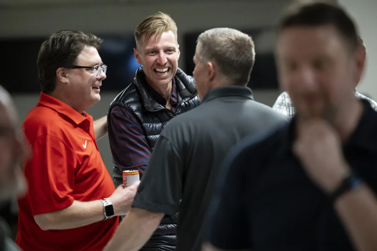 A group of men laugh over drinks at an IT convention. 
