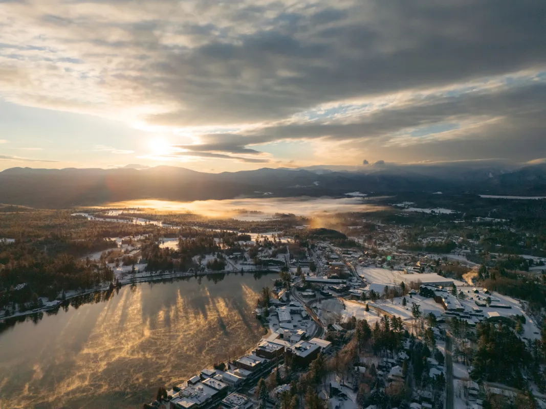 An aerial view of a small, lakeside town in winter on a partly cloudy day at sunrise.