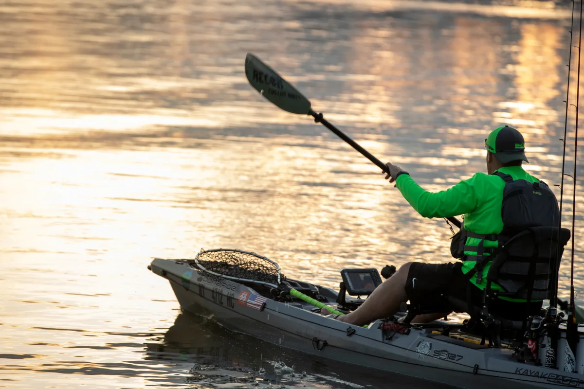 A man fishing from a kayak at sunset.