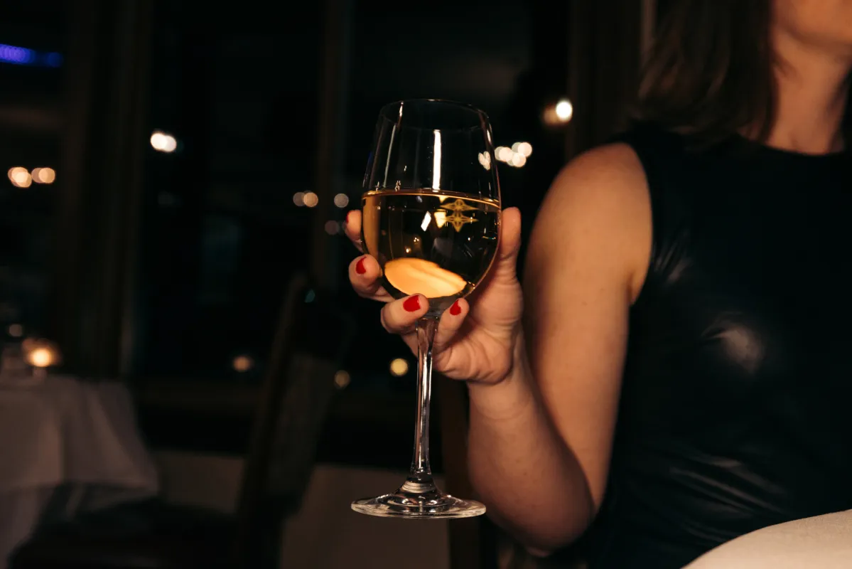 A woman wearing red nail polish holds a glass of wine.