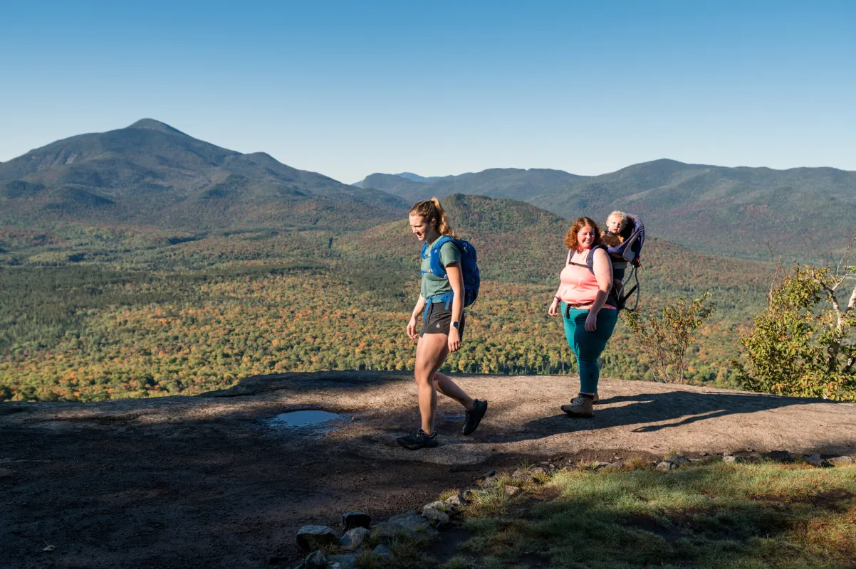 Two adults, one with a baby on her back, hike a ridgeline