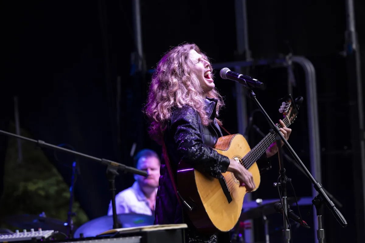 A woman sings with a guitar. 