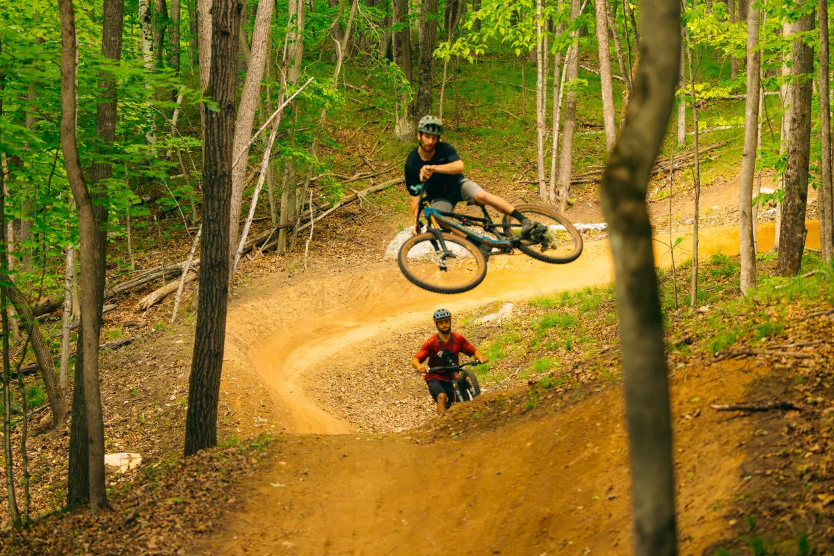 A mountain biker doing a jump on a trail during the summer.