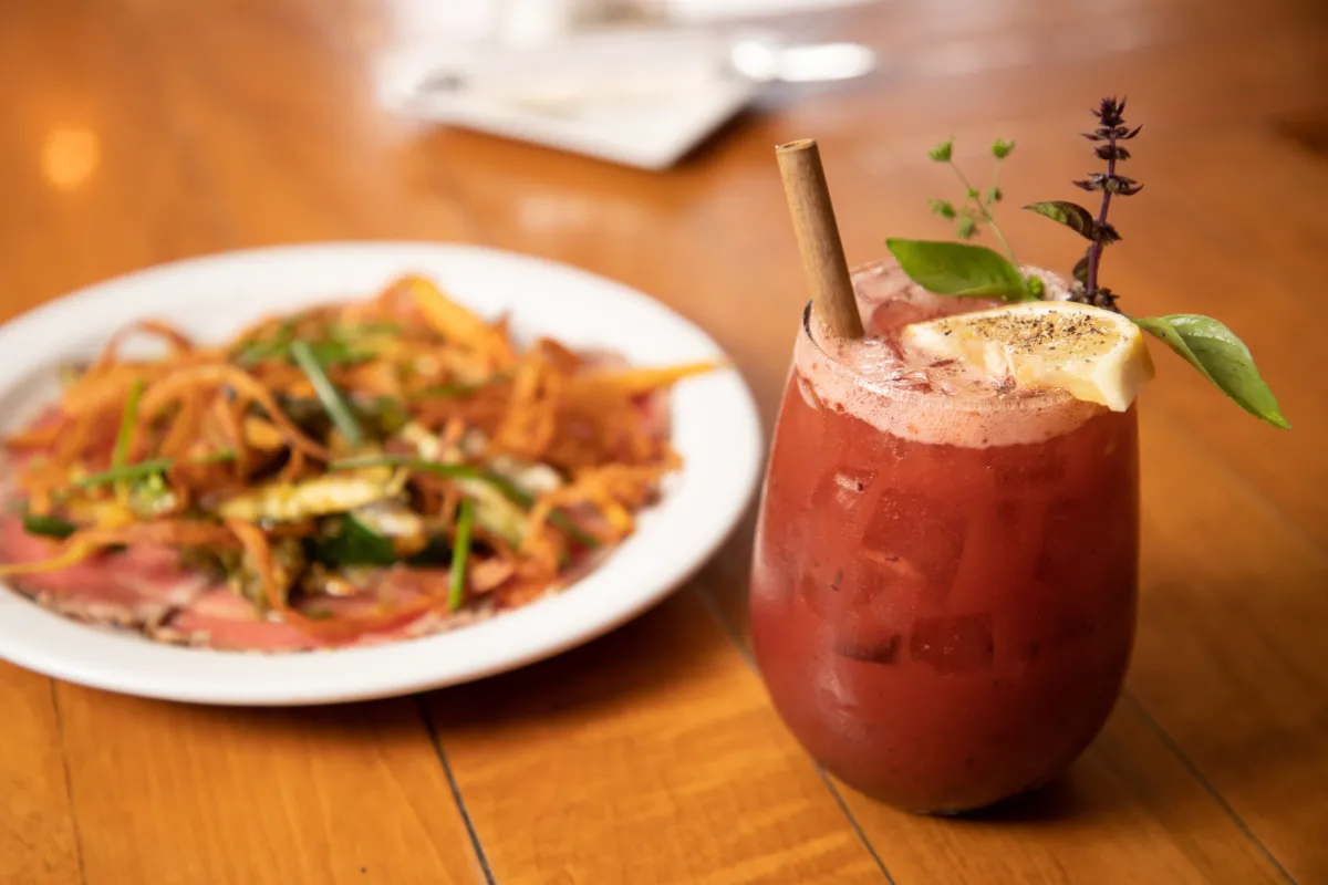 A plate of pasta and vegetables with a fruity cocktail.