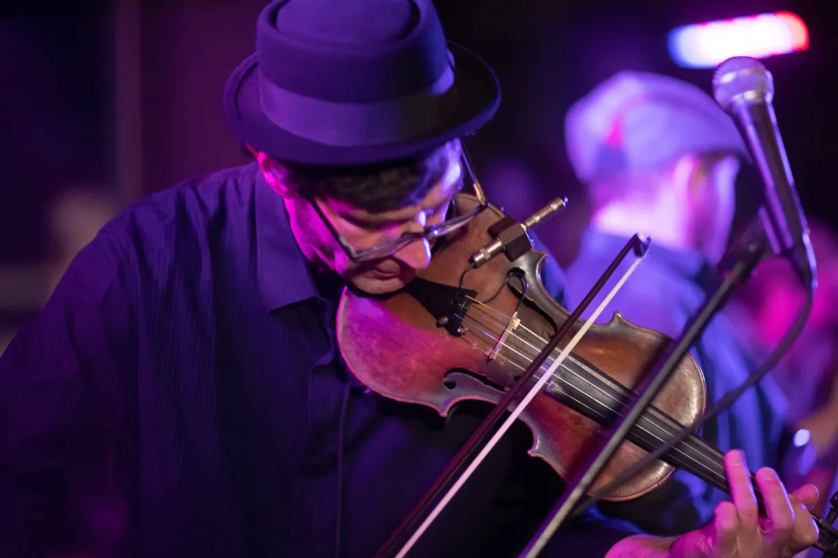 A man plays a fiddle under purple light