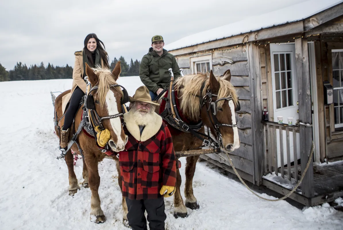 A man and woman ride draft horses in the snow.