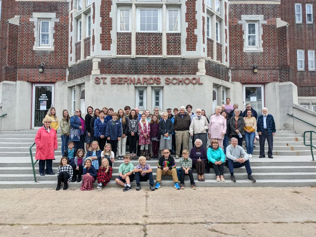 A group of school children sit on the front steps of a catholic school for a picture. 