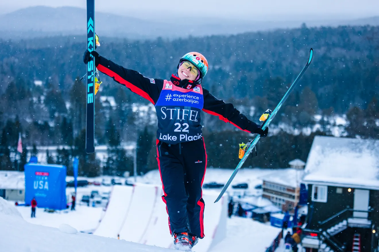 A woman in ski gear smiles and holds up her skis in winter.