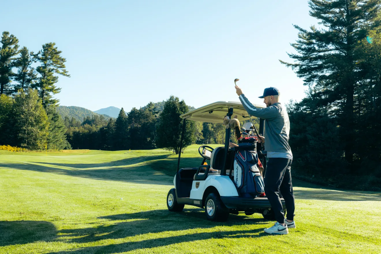 A man retrieves a golf club from a golf cart. 