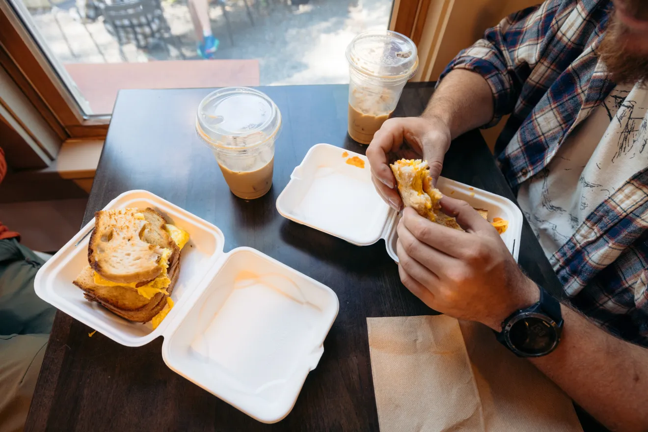 Two men share breakfast sandwiches at a restaurant. 