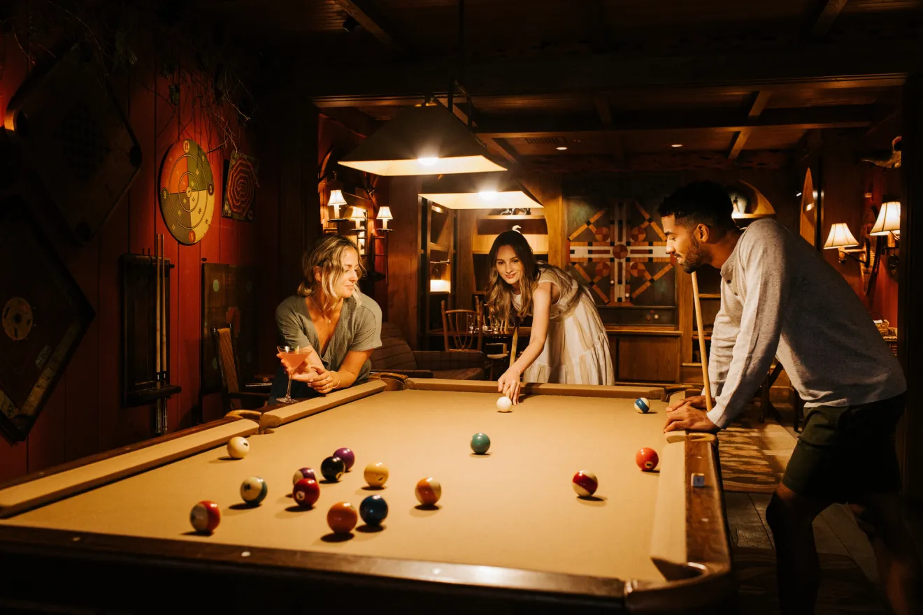 A group of friends play pool in a lodge. 