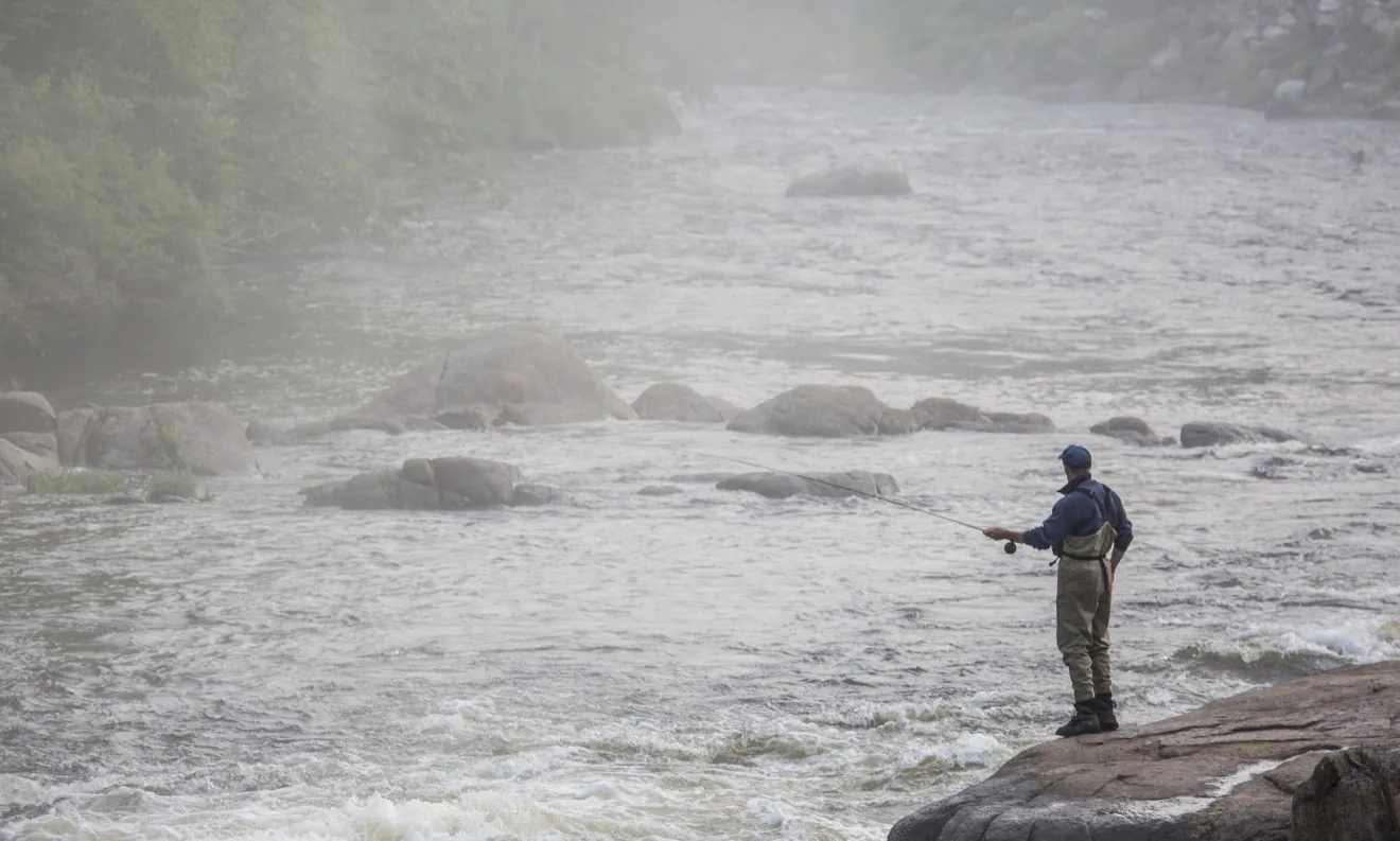 A flyfisher on a rock casting into the morning mist.