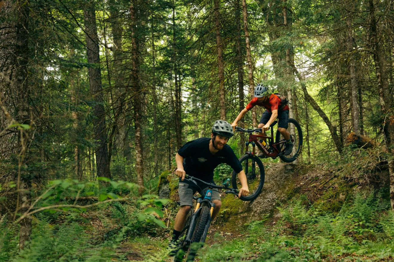 Two men ride mountain bikes on a forest trail. 