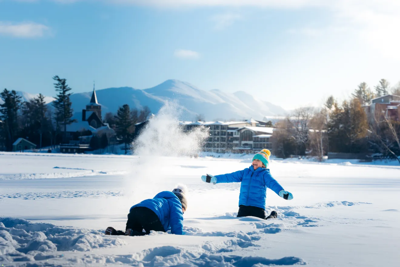 Two kids play in the snow on a frozen lake.