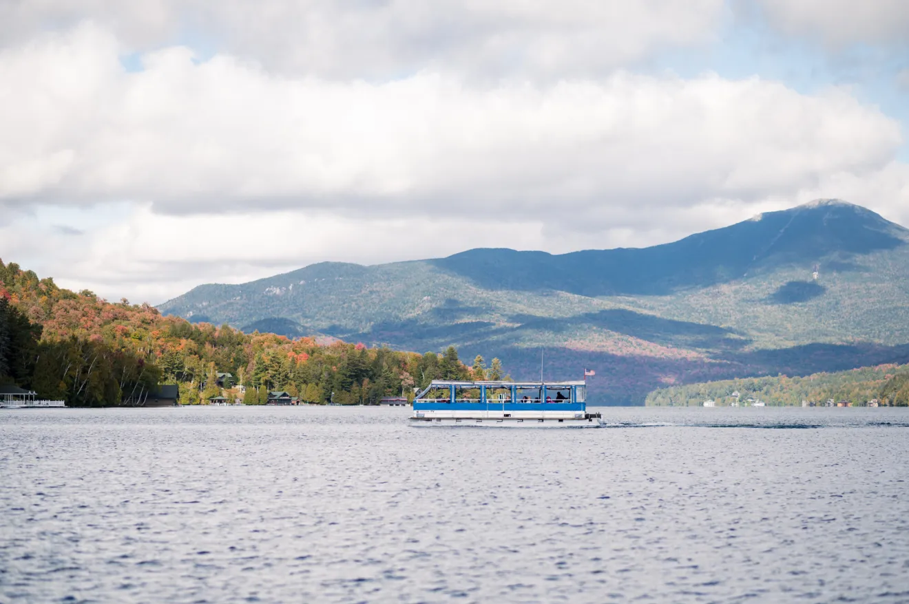 A pontoon boat glides across a lake in fall.